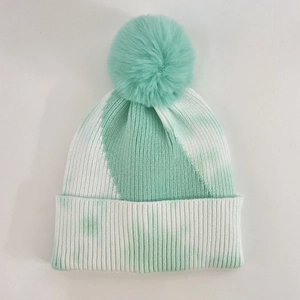 Close-up of tie-dye knit beanie featuring a large faux fur pompom and ribbed cuff details