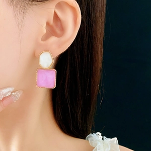 Nahaufnahme goldener Ohrringe mit weißen ovalen und rosa quadratischen Steinen am Model