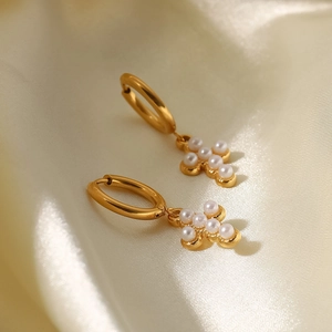 Close-up of gold titanium steel hoop earrings with white pearl cross pendant charm