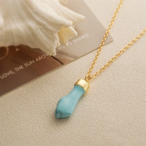 Macro shot of gold chain with blue hand charm on a textured surface with shells