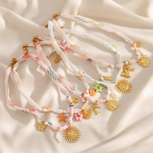 Dettaglio dei ciondoli a conchiglia e sole placcati oro 18K su collane di nastro rosa