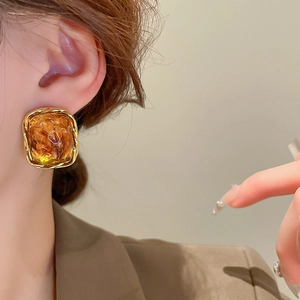 Close-up of elegant amber resin square earring with twisted gold metal border on model