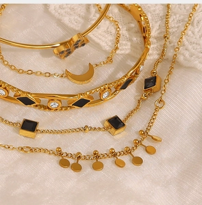 Détail de bracelets dorés empilables avec pierres carrées noires et pendentifs lune