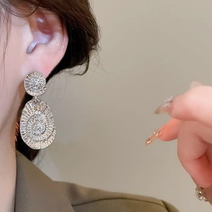 Close-up of silver-toned oval earrings with radiant spiral texture worn by a model