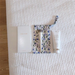 Floral cotton pouch with a 120g face wash and makeup brush on a white quilted surface