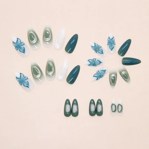 Detail of almond-shaped press-on nails with green lily patterns and silver 3D relief
