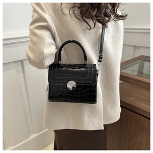 Détail d'un sac à main noir brillant à motif crocodile avec fermoir argenté sur manteau