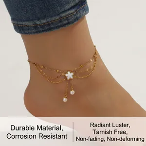 Detail of layered gold anklet with white shell flower charm and pearl tassels on a beach