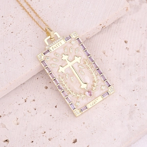 Close-up of gold cross pendant with pink and purple stones and FAITH engraving