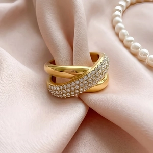 Macro shot of gold crisscross ring with pavé diamonds on elegant pink silk background