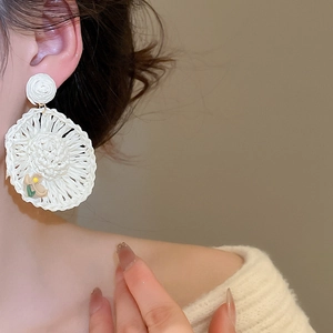 Close-up of white woven raffia drop earrings with 3D floral accents on a model