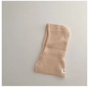 Detailed knit texture of beige baby balaclava hat with dual buttons and a side brand label