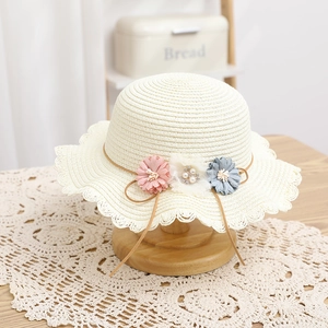 Dettaglio ravvicinato di un cappello di paglia bimbi con tre fiori su supporto legno