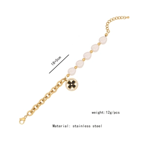 Detail of a gold stainless steel bracelet with a black clover pendant and baroque pearl