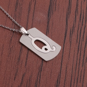Gros plan d'un collier en acier argenté avec pendentif rectangulaire ajouré sur bois