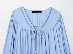 Detailopname van lichtblauwe blouse met V-hals, kanten rand en geplooide textuurdetails