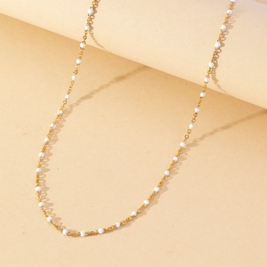 Detailed shot of a delicate gold-plated chain necklace featuring tiny white enamel beads