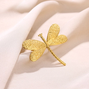 Detailed close-up of golden dragonfly brooch with intricate textured wings on silk fabric