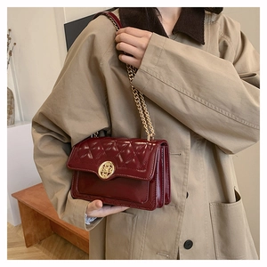 Detail of wine red quilted shoulder bag with gold hollow clasp on khaki trench coat