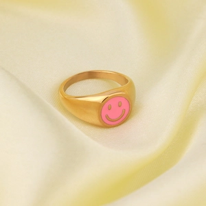 Close-up of golden smiley face ring with pink enamel on yellow satin background