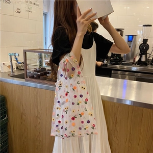 Detail of white mesh tote bag with colorful floral embroidery in a cafe setting