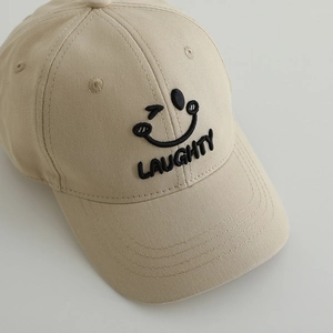 Close-up of embroidered winking smiley face and LAUGHTY text on a beige cotton baseball cap