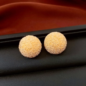 Close-up of golden round stud earrings with unique frosted sand texture on black leather