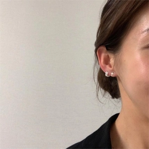 Gros plan d'un clou d'oreille croix en argent et d'un anneau texturé sur l'oreille