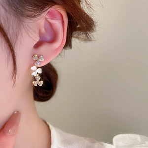 Detail view of a model wearing triple clover dangle earrings with zircon and white enamel