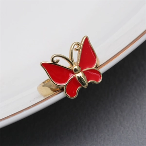 Macro shot of a red butterfly enamel ring with golden edges resting on a white ceramic plate
