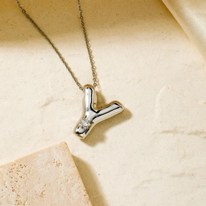 Silver Y letter balloon pendant necklace with sparkling zircon on textured stone surface