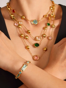 Detail of layered gold necklaces with colorful faceted glass stones on a black background