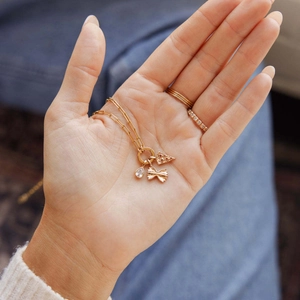 Gold necklace featuring pizza, farfalle pasta, and gemstone pendants on a palm