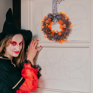 Halloween wreath with orange pumpkin heads and black glitter tinsel on white door