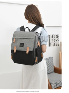 Rear view of a grey and black diaper backpack with texture leather handles on a model