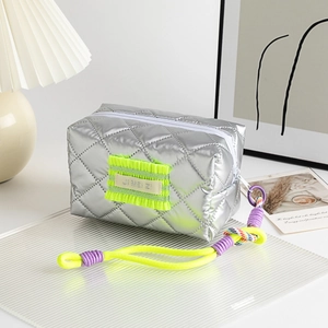 Détail de la trousse de maquillage matelassée argentée avec patch néon et sangle tressée