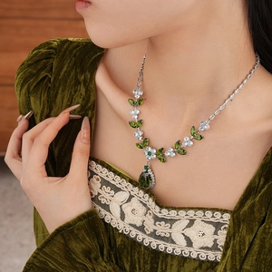 Detailed view of silver necklace with green leaf stones and pear-shaped pendant on neck