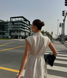 Outdoor street view showing the fabric texture and waist tie of a beige sleeveless dress