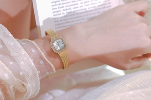 Close-up of gold square rhinestone watch worn by model with elegant lace details