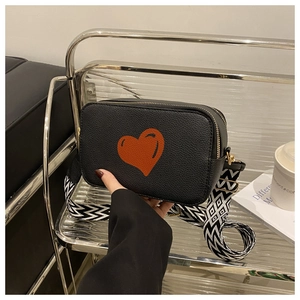 Detail of black lychee grain leather crossbody bag with red heart and geometric strap