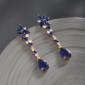 Detail of luxury gold earrings featuring teardrop blue crystals and sparkling zircons