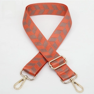 Detail of adjustable coral orange jacquard bag strap with golden metal hardware