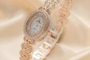 Close-up of rose gold oval watch with crystal-encrusted leaf band on silk fabric