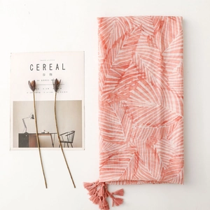 Close-up of pink and white leaf pattern scarf with tassel details on a white surface
