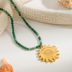 Detail of gold sun pendant on green beaded necklace with decorative seashells