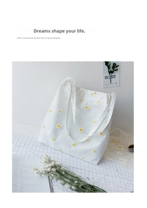 Close-up of a white canvas tote bag with yellow daisy embroidery in a lifestyle setting