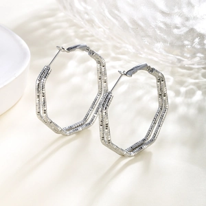 Close-up of silver hexagonal hoop earrings with engraved texture on ripple glass background