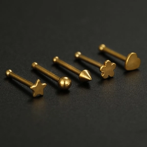 Five gold stainless steel nose studs in star, heart, and flower shapes on black background