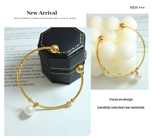 Detail of a gold open bangle with geometric beads and a white pearl charm on a candle