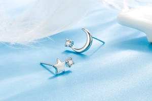 Detailed close-up of asymmetric star and moon stud earrings on soft blue silk fabric